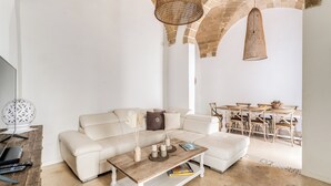 A modern living room with a white sofa, a wooden coffee table, and a dining area with a table and chairs.