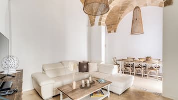 Ein modernes Wohnzimmer mit einem weißen Sofa, einem Holztisch und einem Essbereich mit Tisch und Stühlen.