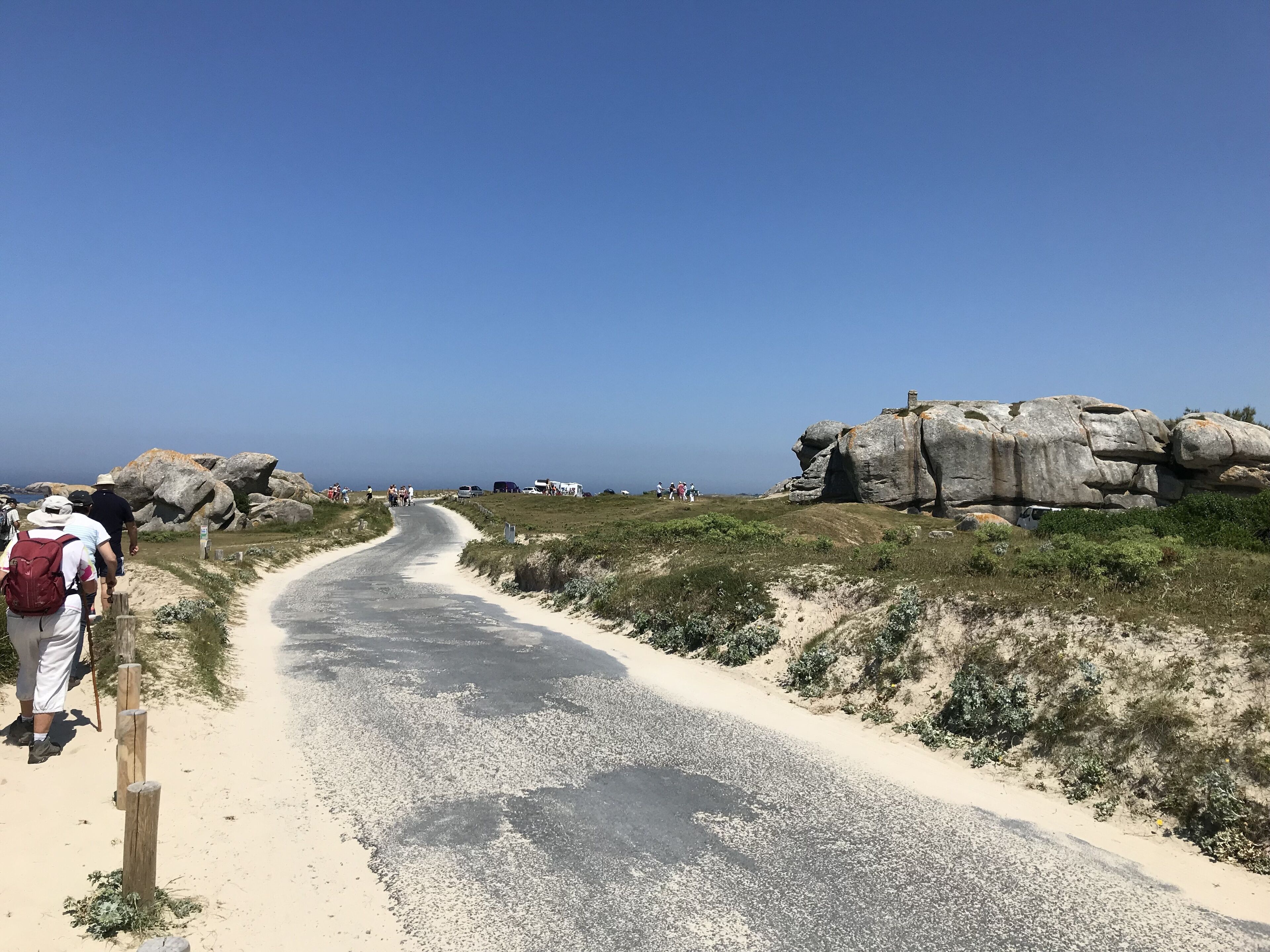 A paved path leading to a rocky area with large boulders and a clear blue sky.