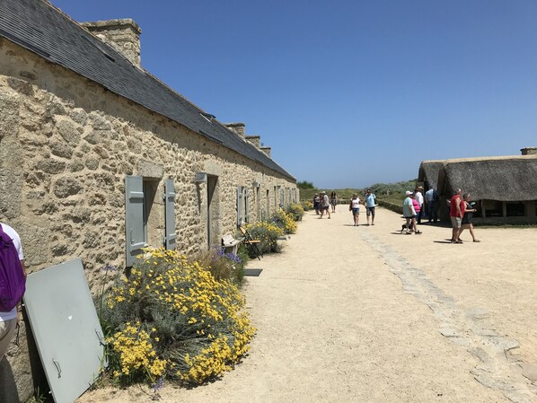 A stone building with a thatched-roof structure, a dirt path, and visitors.