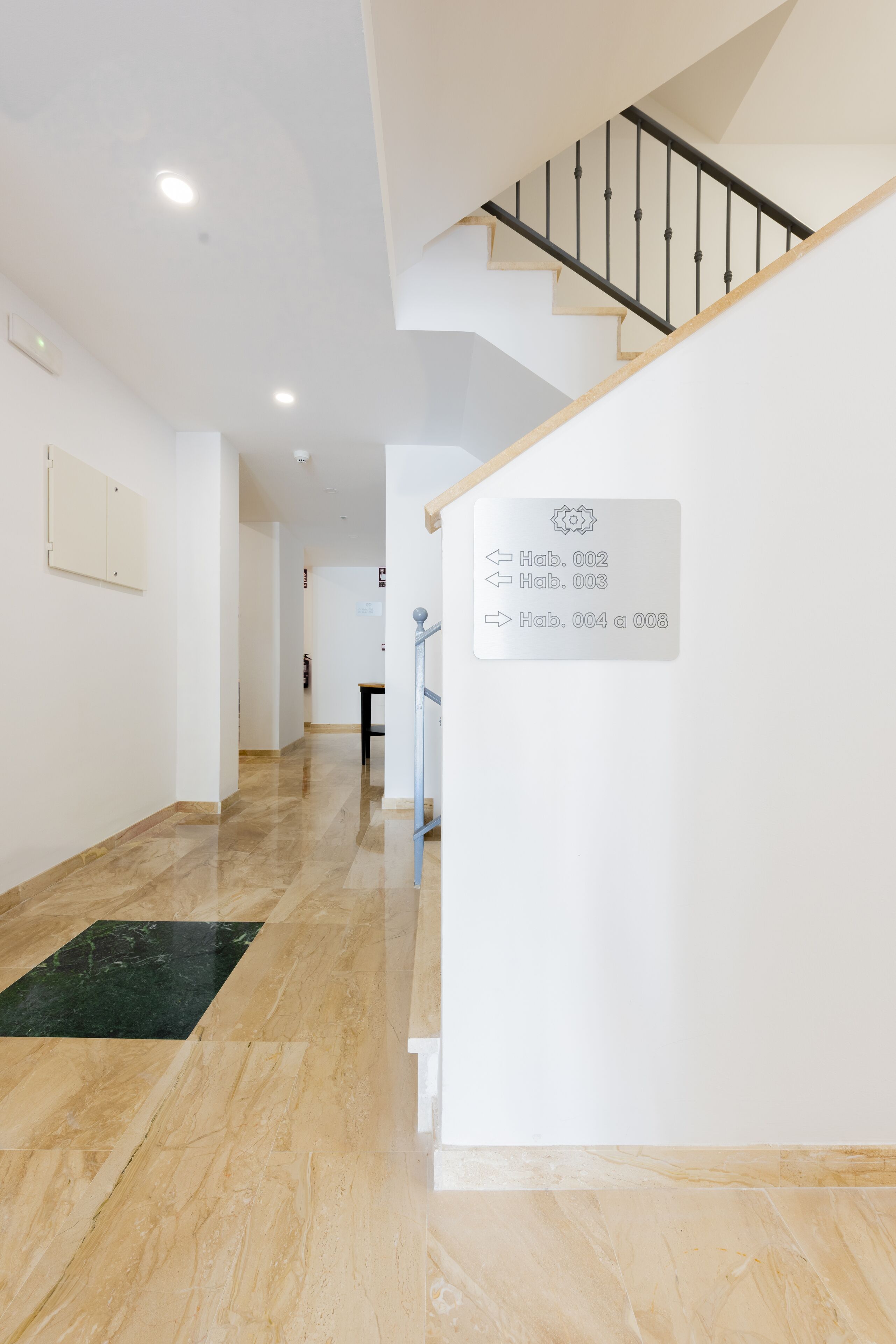 A spacious hallway with a polished marble floor, a staircase with a wooden handrail, and a sign indicating room numbers.