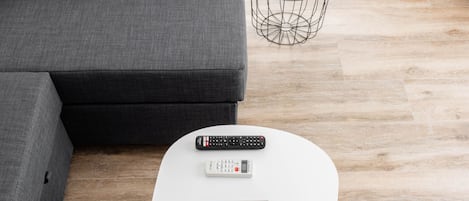 A modern living room with a grey sofa, a white coffee table with a picture frame, a remote control, and a small plant on a round side table.