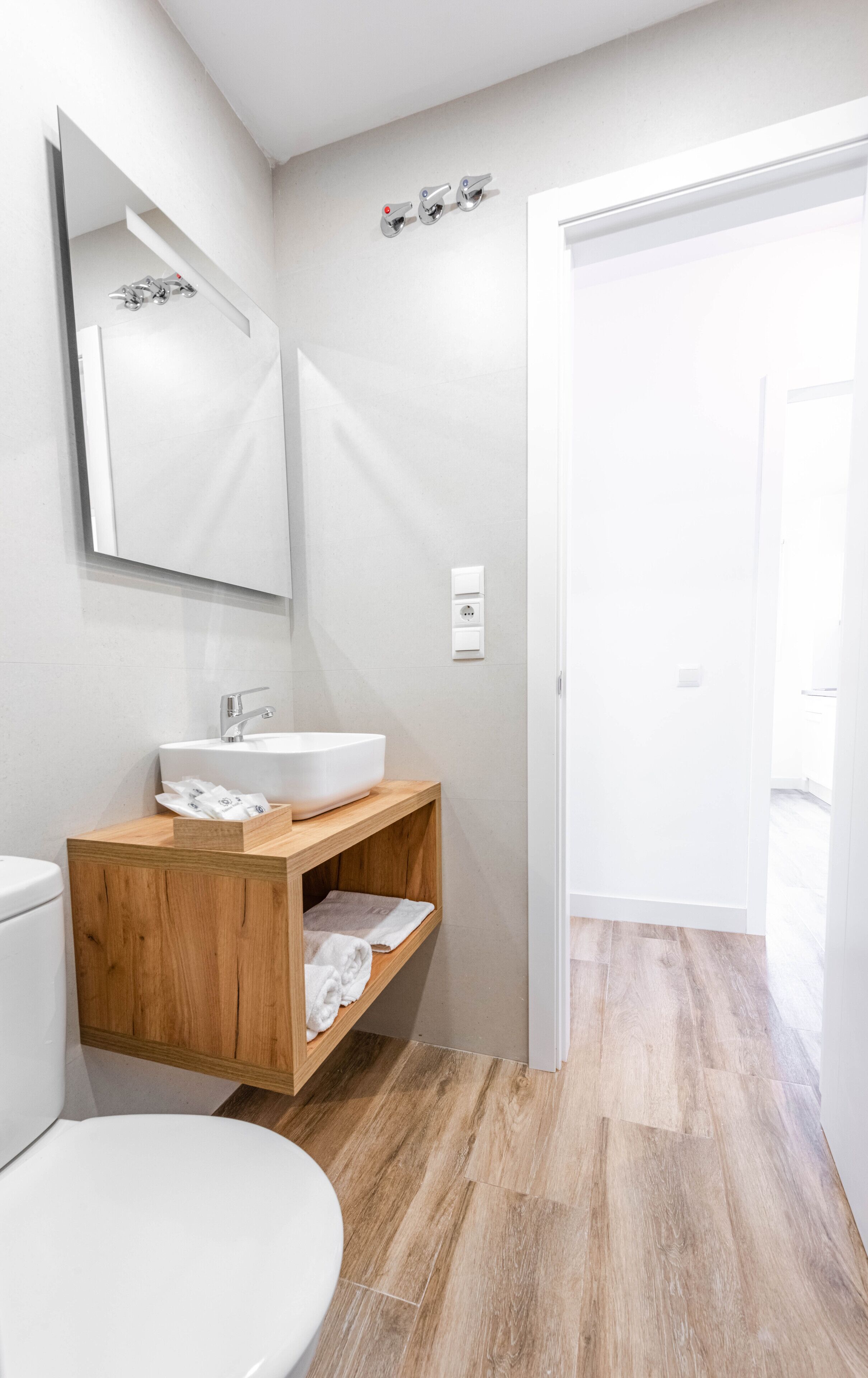 Un baño moderno con lavamanos blanco, tocador de madera y un espejo grande.