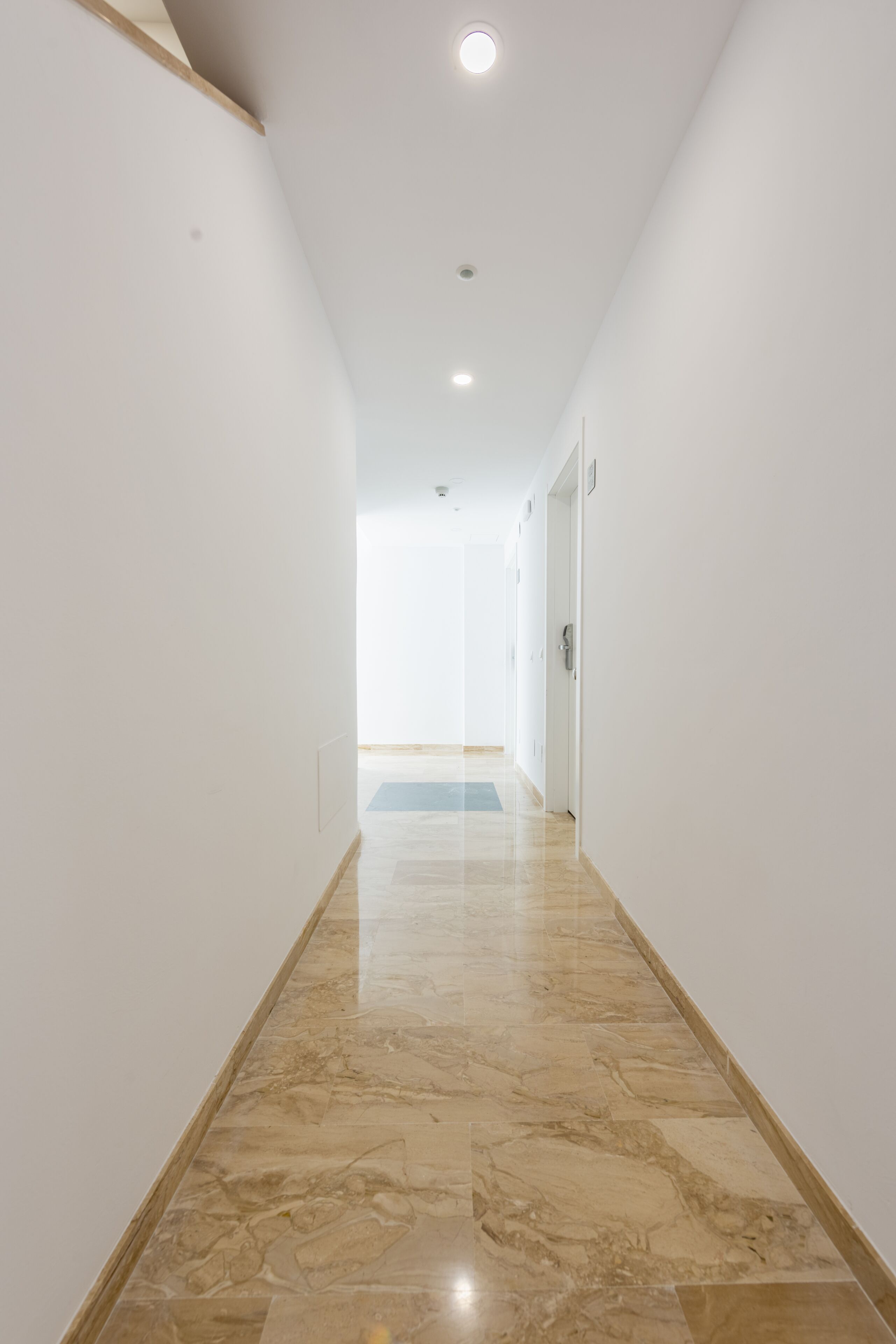 A hallway with white walls and a marble floor leading to a door.