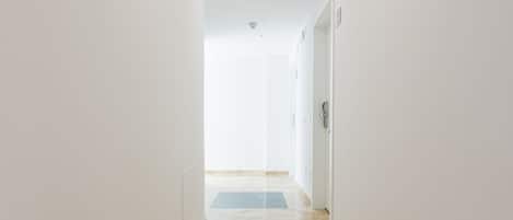 A hallway with white walls and a marble floor leading to a door.