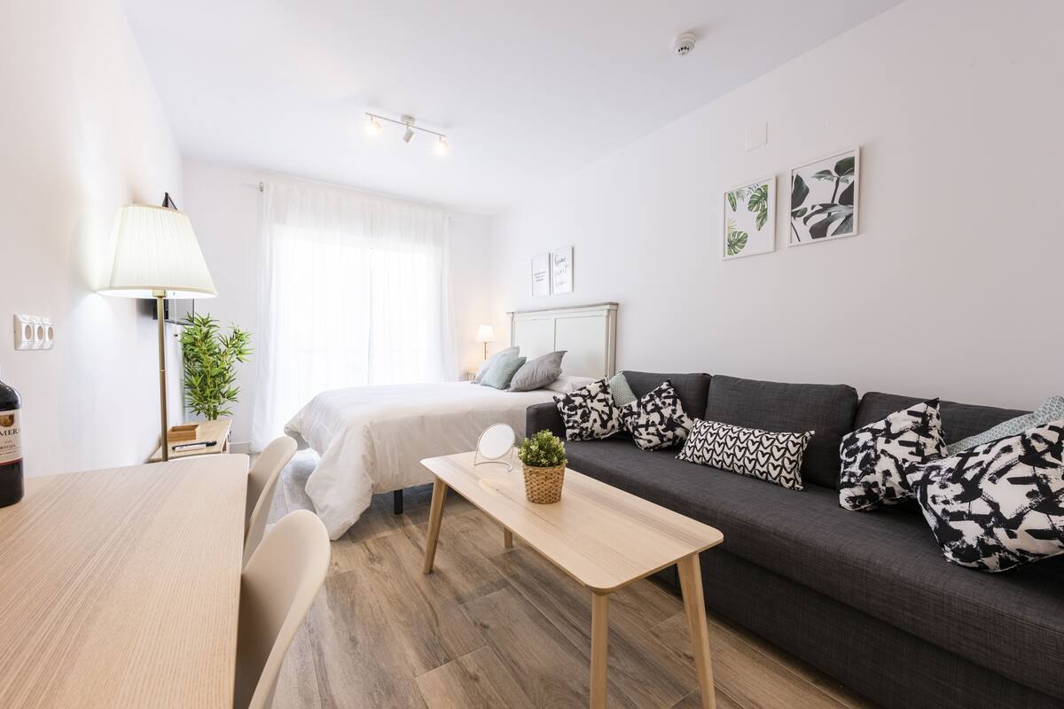 Een moderne, goed verlichte woonruimte met een bank, een klein tafeltje en een bed.