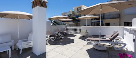 A rooftop patio with white lounge chairs, umbrellas, and a tiled floor.