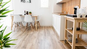 Eine moderne Küche mit weißen Schränken, einer Mikrowelle und einer Kaffeemaschine. Es gibt einen Essbereich mit Tisch und Stühlen.