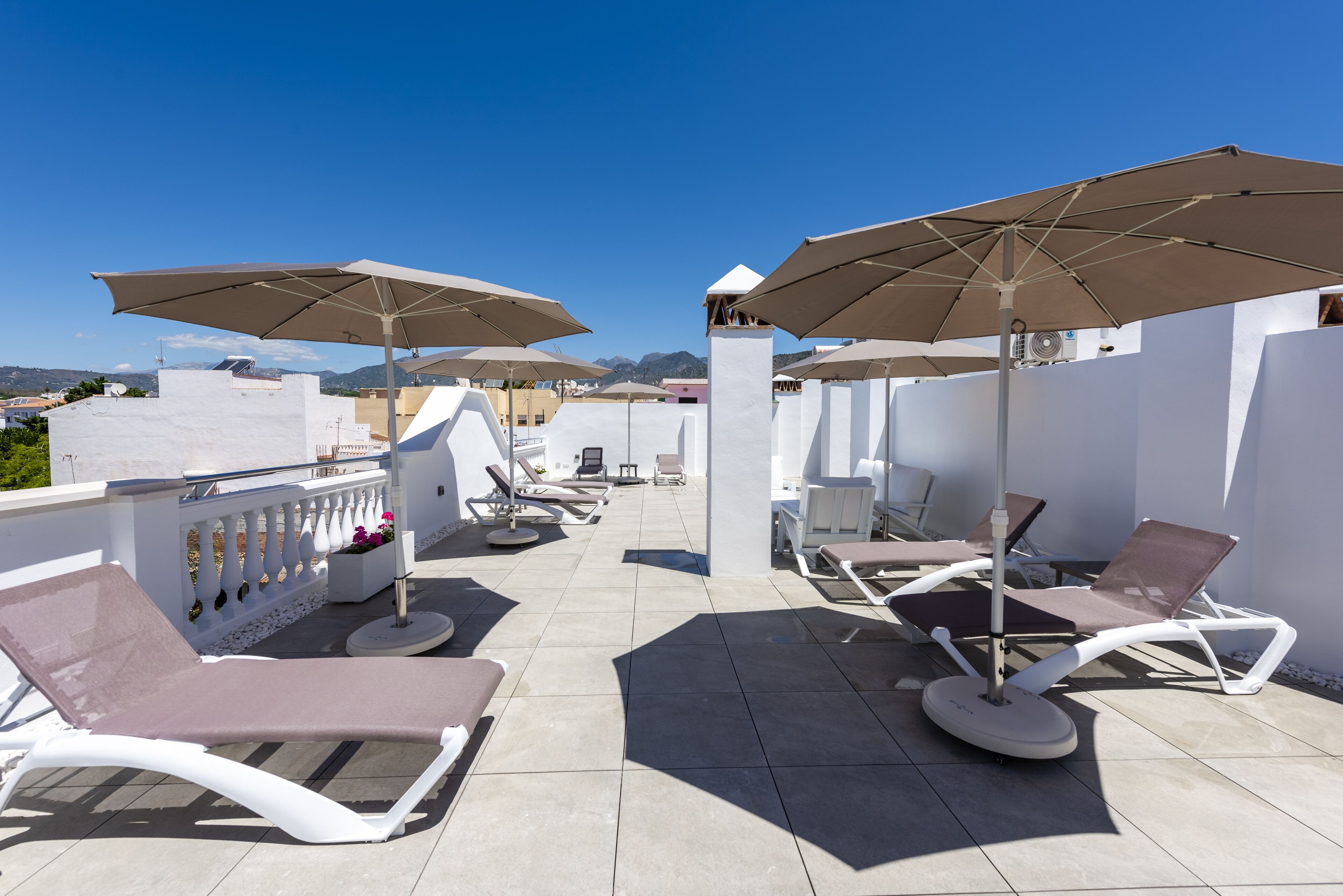 Terraza en la azotea con sillones de sol y sombrillas, con vistas a la ciudad y las montañas.