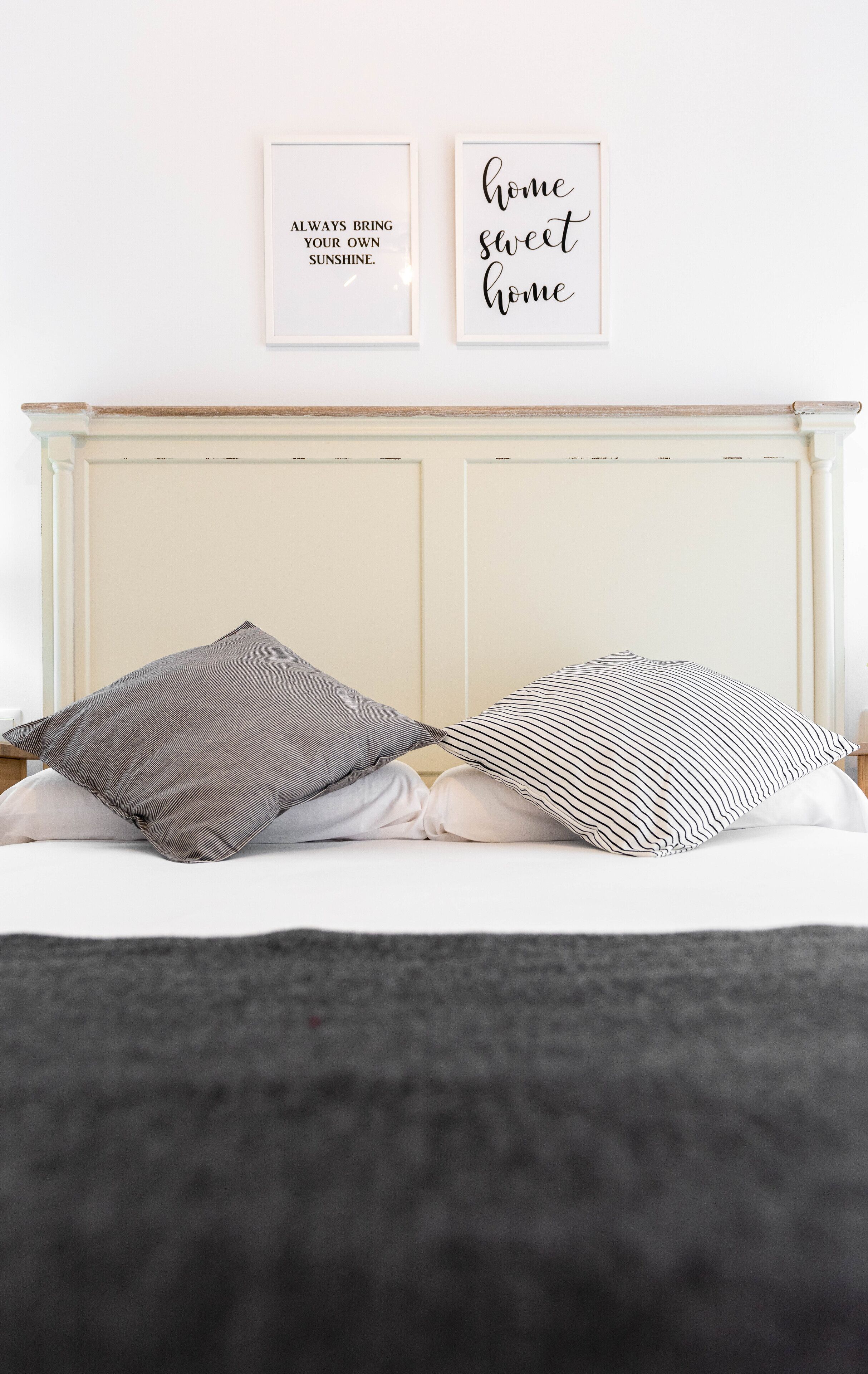 A bed with two pillows, a white headboard, and two framed quotes on the wall.