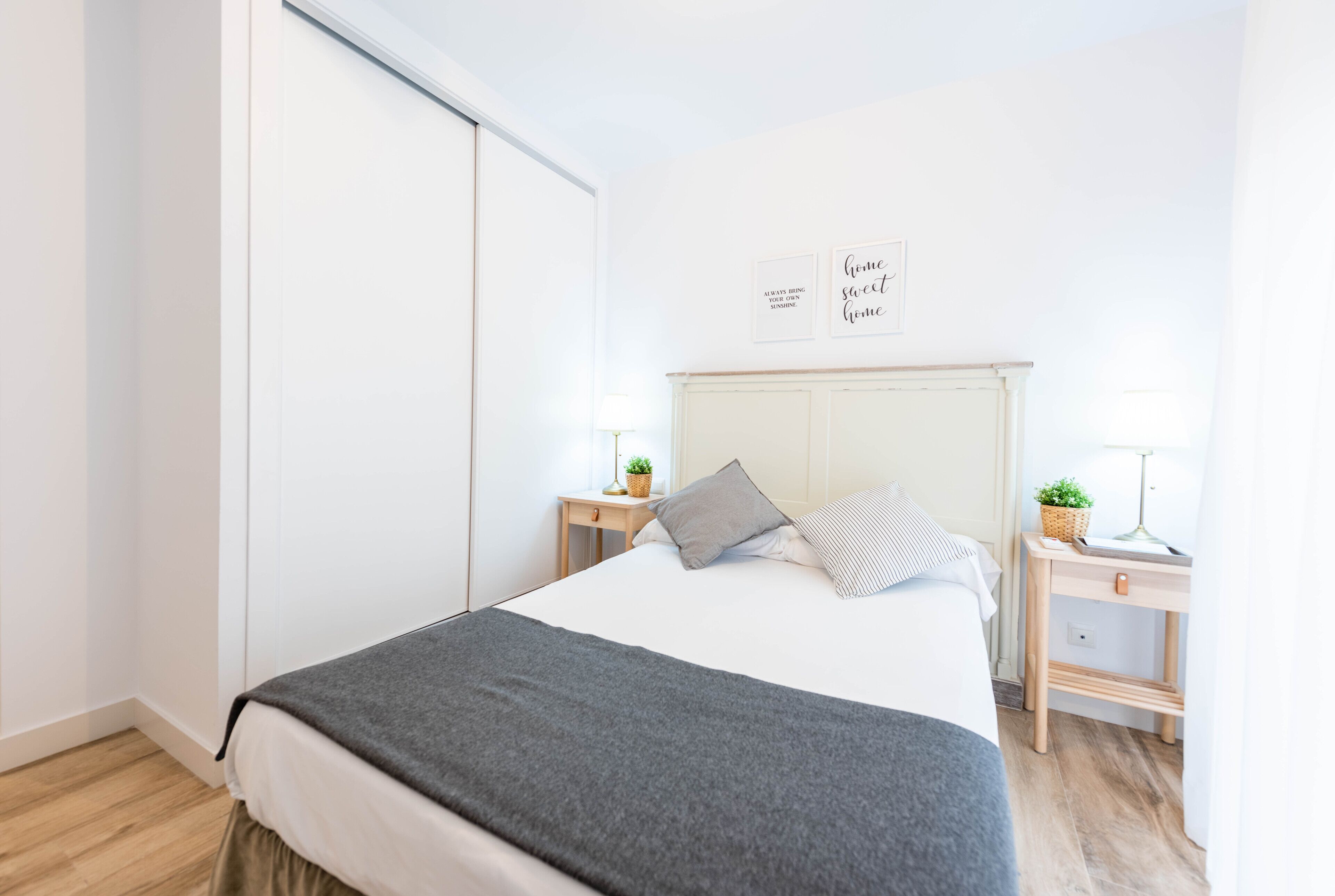 A bedroom with a bed, bedside tables, a nightstand, a lamp, a wall with two framed signs, and a sliding door.