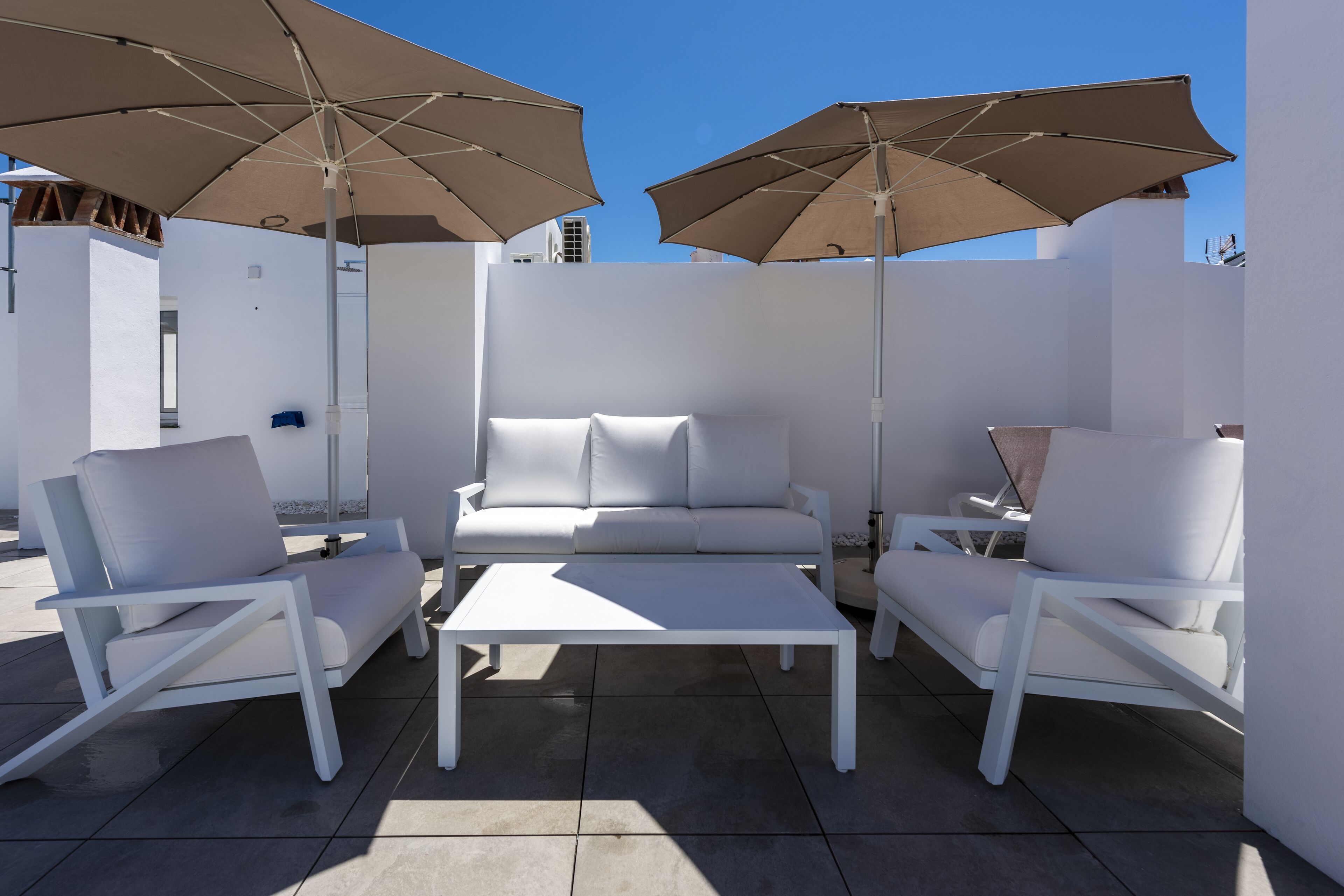 A modern outdoor seating area with white furniture and large umbrellas.