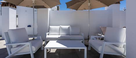 A modern outdoor seating area with white furniture and large umbrellas.