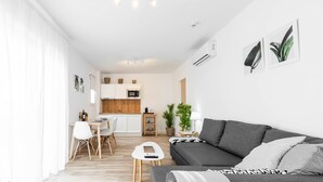 Ein modernes Wohnzimmer mit einem grauen Sofa, einem kleinen weißen Tisch und einer Küche im Hintergrund.