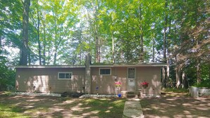 A single-story cabin with a front porch, surrounded by trees. - The Lodge in Manistee (Manistee)