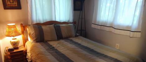 Un dormitorio con cama, mesita de noche con lámpara y cortinas en las ventanas.