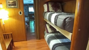 A narrow hallway with wooden flooring leading to a bunk bed area with a wooden headboard and a bedside table. - The Lodge in Manistee (Manistee)