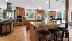 A spacious kitchen with wooden cabinets, a large island with bar stools, stainless steel appliances, and pendant lighting.