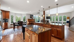 A spacious kitchen with wooden cabinets, a granite countertop, and a dining area with a piano.