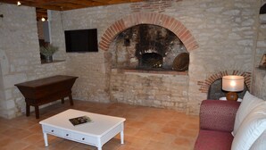 Una sala de estar acogedora con pared de piedra, chimenea, una mesa de centro blanca, un banco de madera y un sofá estampado.