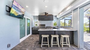 A modern kitchen with a large island, bar stools, a ceiling fan, and a view of the outdoors. - 🌺Urlaub Haus | A Lakefront Paradise Reimagined in Murex Lakes🐬 (Sanibel)