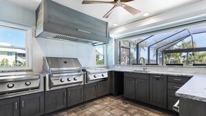 A modern kitchen with a large island, built-in appliances, and a large window providing a view of the outdoors. - 🌺Urlaub Haus | A Lakefront Paradise Reimagined in Murex Lakes🐬 (Sanibel)