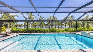 A swimming pool with a clear view of a lake, surrounded by palm trees and a covered area with chairs. - 🌺Urlaub Haus | A Lakefront Paradise Reimagined in Murex Lakes🐬 (Sanibel)