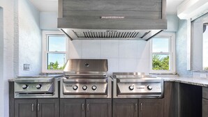 A kitchen with three stainless steel stoves, dark wooden cabinets, and a vent hood. - 🌺Urlaub Haus | A Lakefront Paradise Reimagined in Murex Lakes🐬 (Sanibel)
