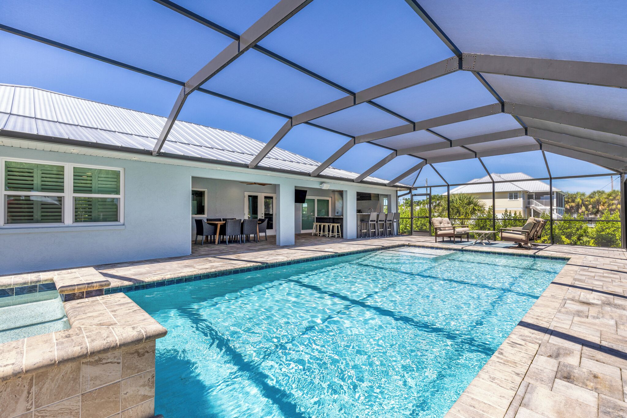 A swimming pool with a covered patio area, a white building with green shutters, and a clear blue sky.