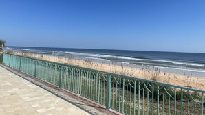 A beach view with a metal railing and a paved walkway.