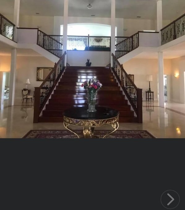 Un hall d’entrée spacieux, agrémenté d’un magnifique escalier, d’une table décorative et d’un vase rempli de fleurs.