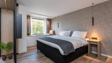A modern bedroom with a large bed, bedside tables, a window with curtains, and a plant.