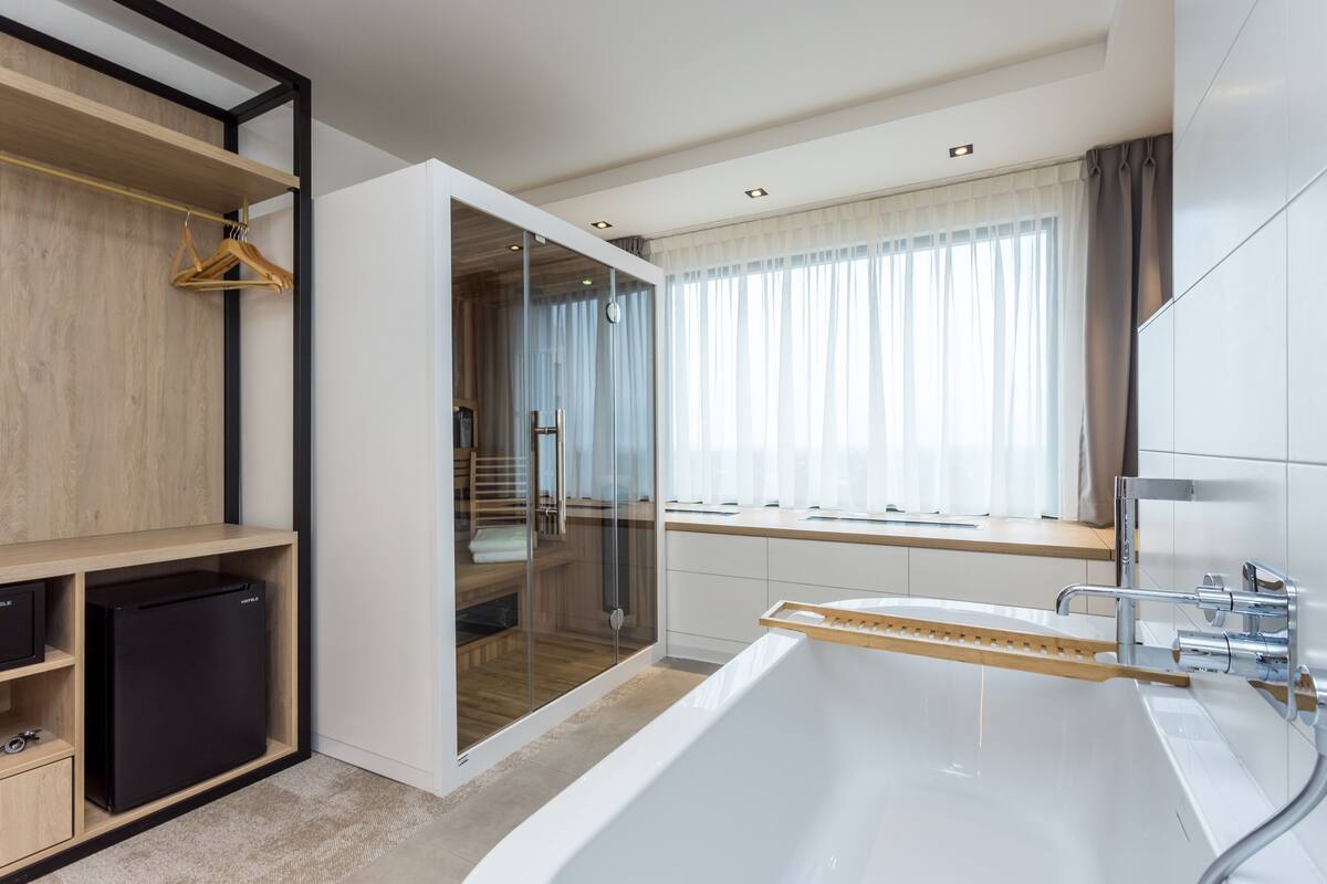Un baño moderno con una bañera independiente, cabina de ducha de vidrio y una ventana con cortinas.