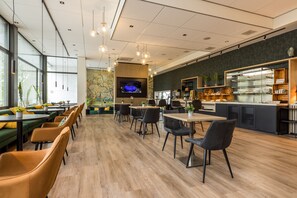 Ein modernes Café mit Holzboden, schwarzen und gelben Stühlen, einem Fernsehbildschirm und einer Theke mit Backwaren.