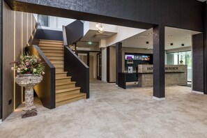 A modern hotel lobby with a staircase, a reception desk, and a flower arrangement.