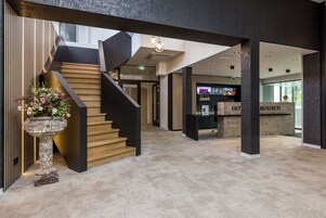 Un moderno vestíbulo de hotel con una escalera, una recepción y un arreglo floral.