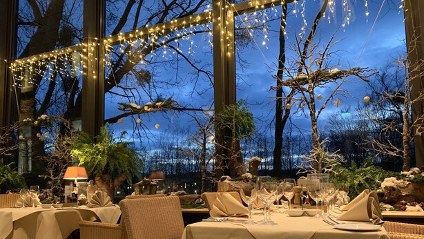 Un área de comedor al aire libre con mesas dispuestas para una comida, rodeada de árboles y luces colgantes.