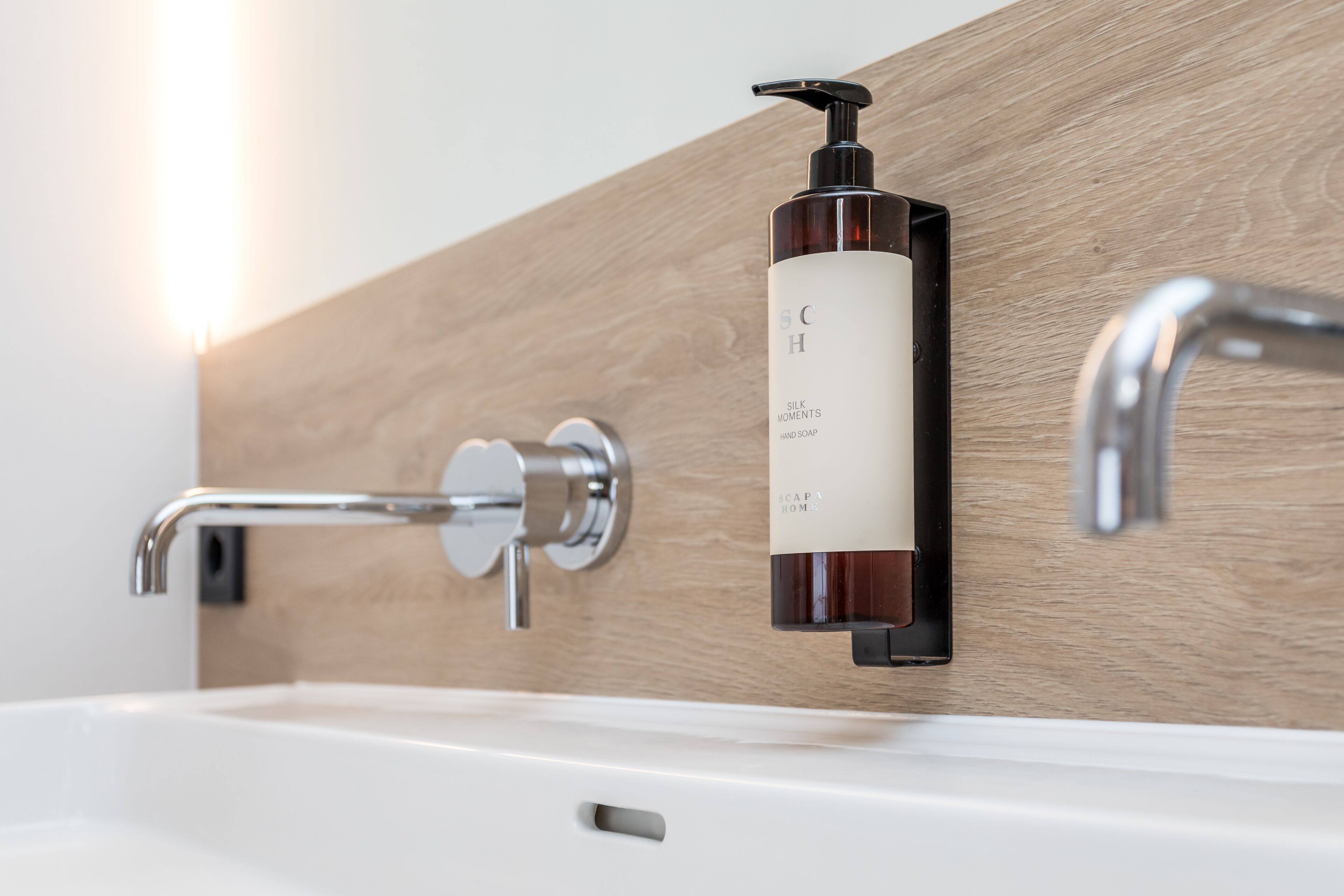 A modern bathroom with a wooden wall, a white sink, and a hand soap dispenser.