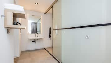 Un baño moderno con cabina de ducha de vidrio, estante de madera con artículos de aseo, lavamanos y espejo.