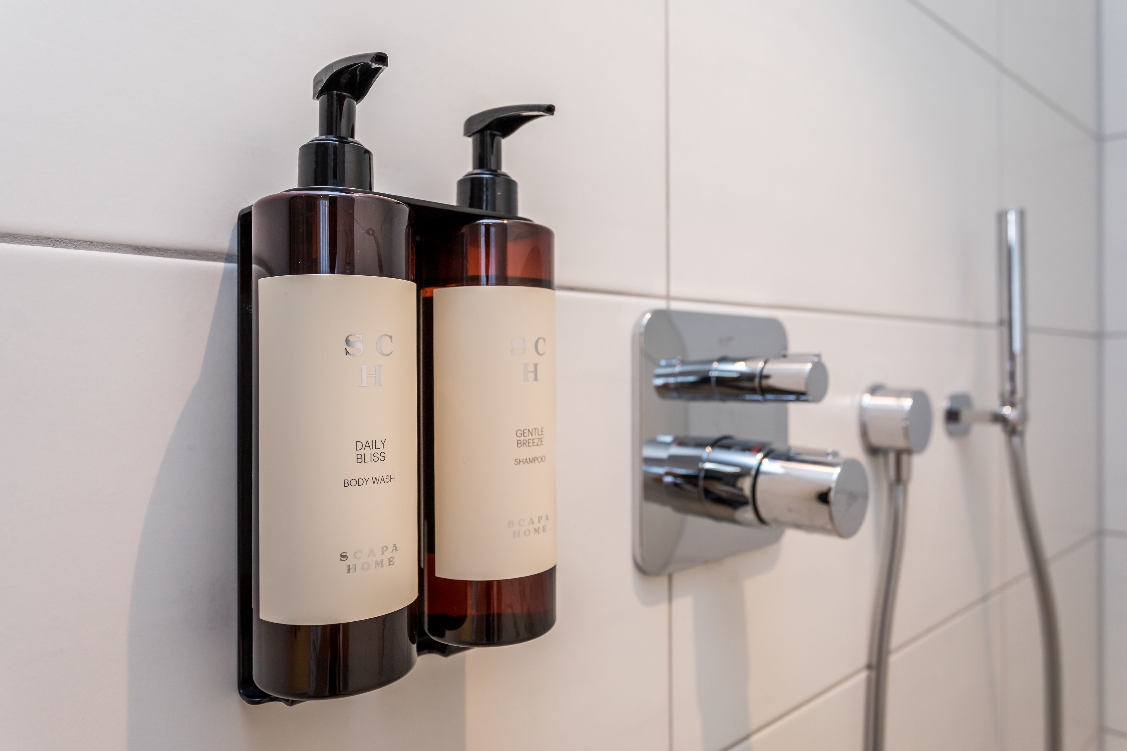 Two bottles of body wash and shampoo on a bathroom wall.