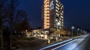 Un hotel moderno con señalización iluminada, una entrada bien iluminada y un área exterior ajardinada.
