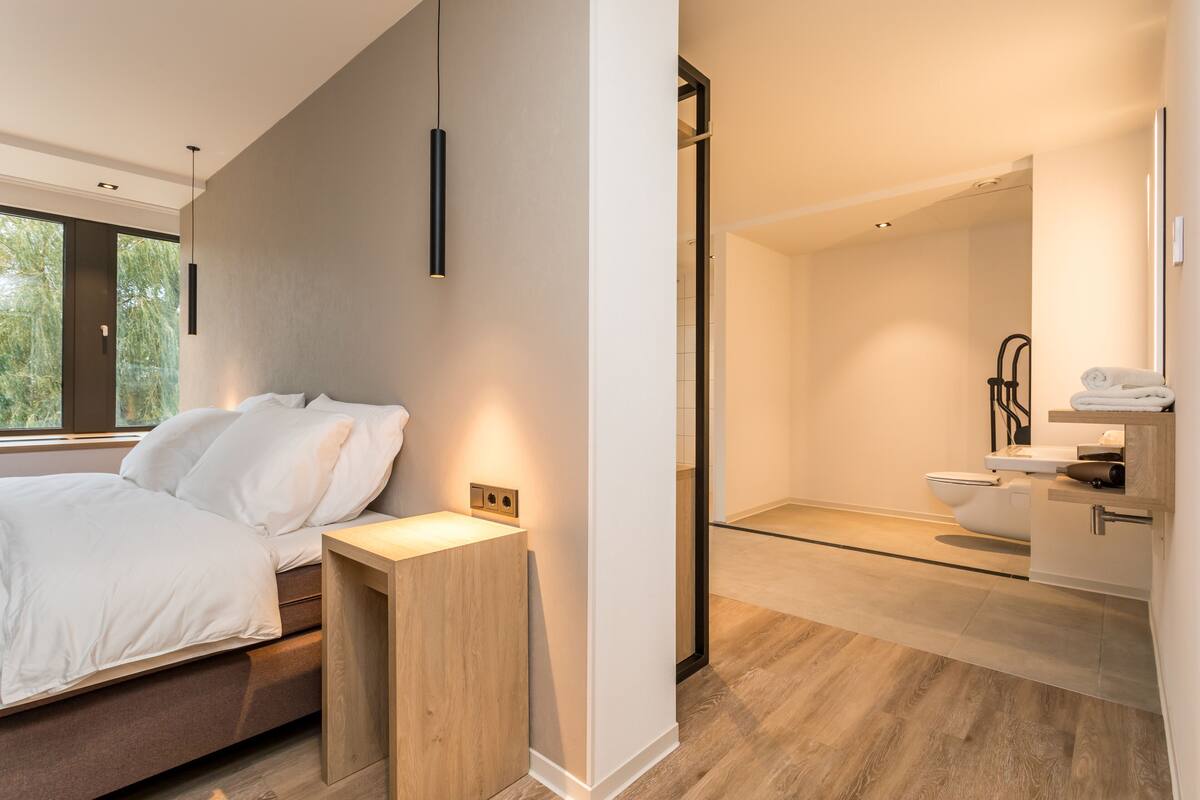 Un dormitorio moderno con cama, mesita de noche y vistas al baño.