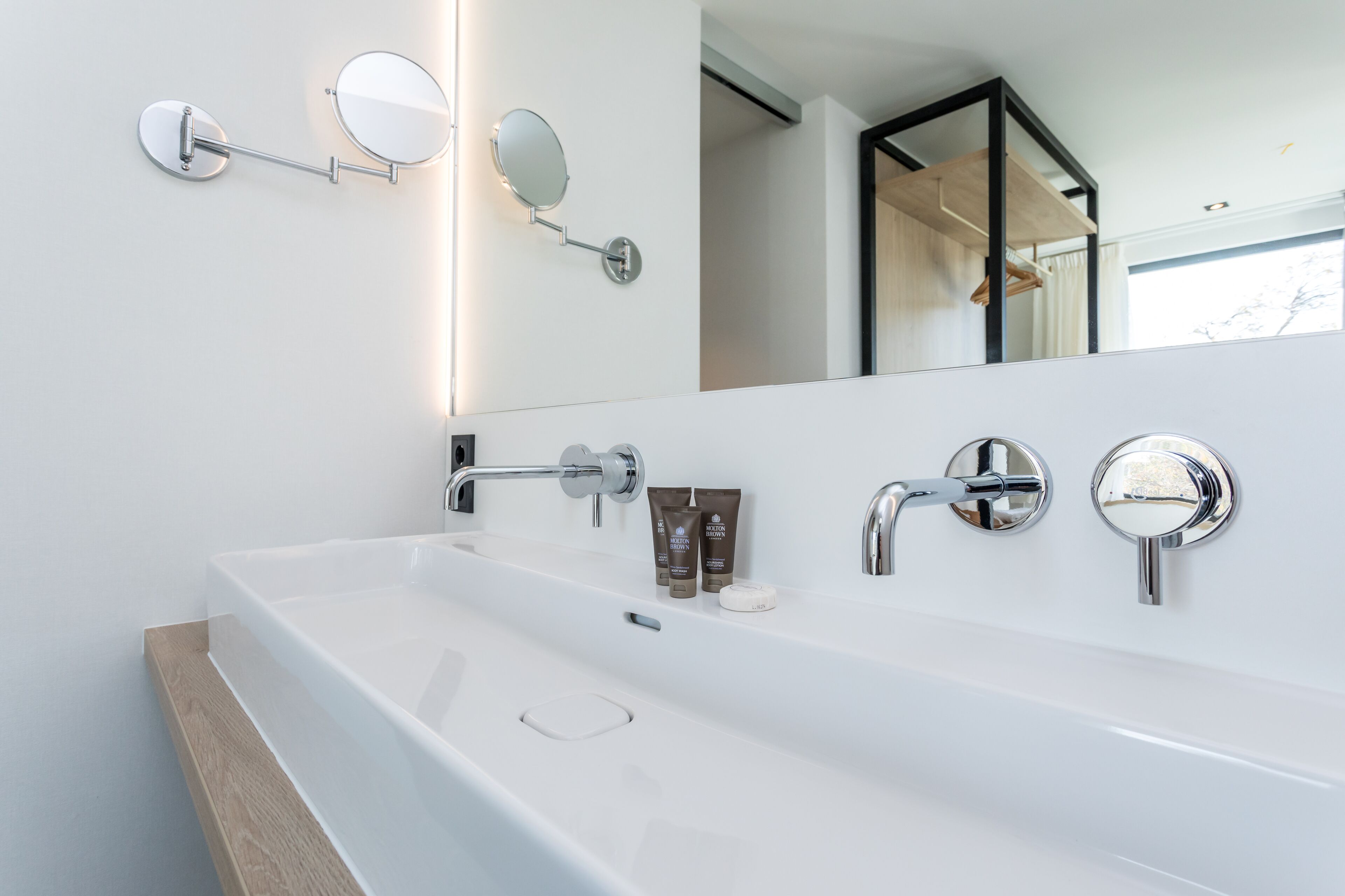 Un baño moderno con un lavabo blanco grande, dos espejos redondos y una encimera de madera.