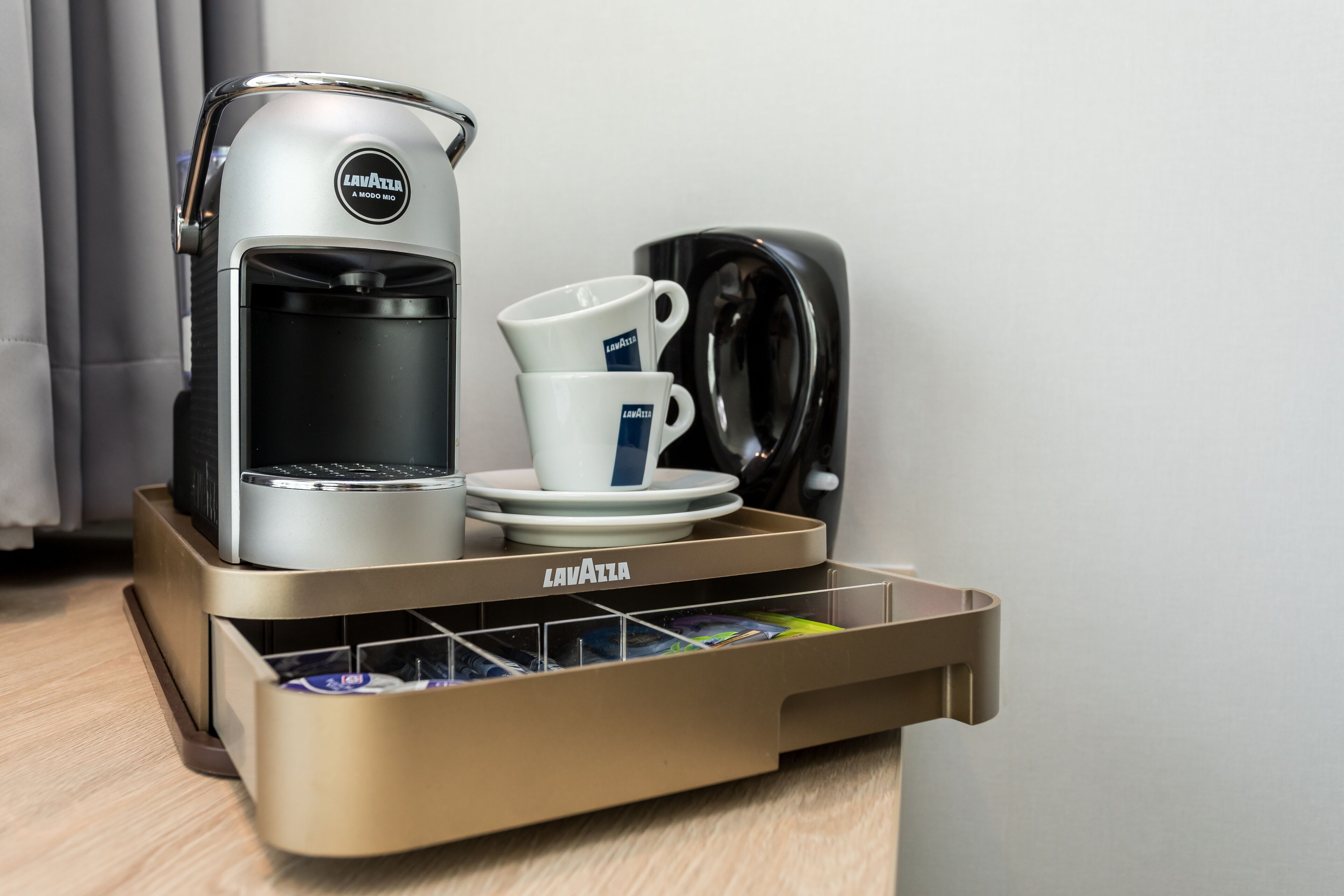 Una cafetera, una taza y una bandeja con un soporte para cápsulas de café.