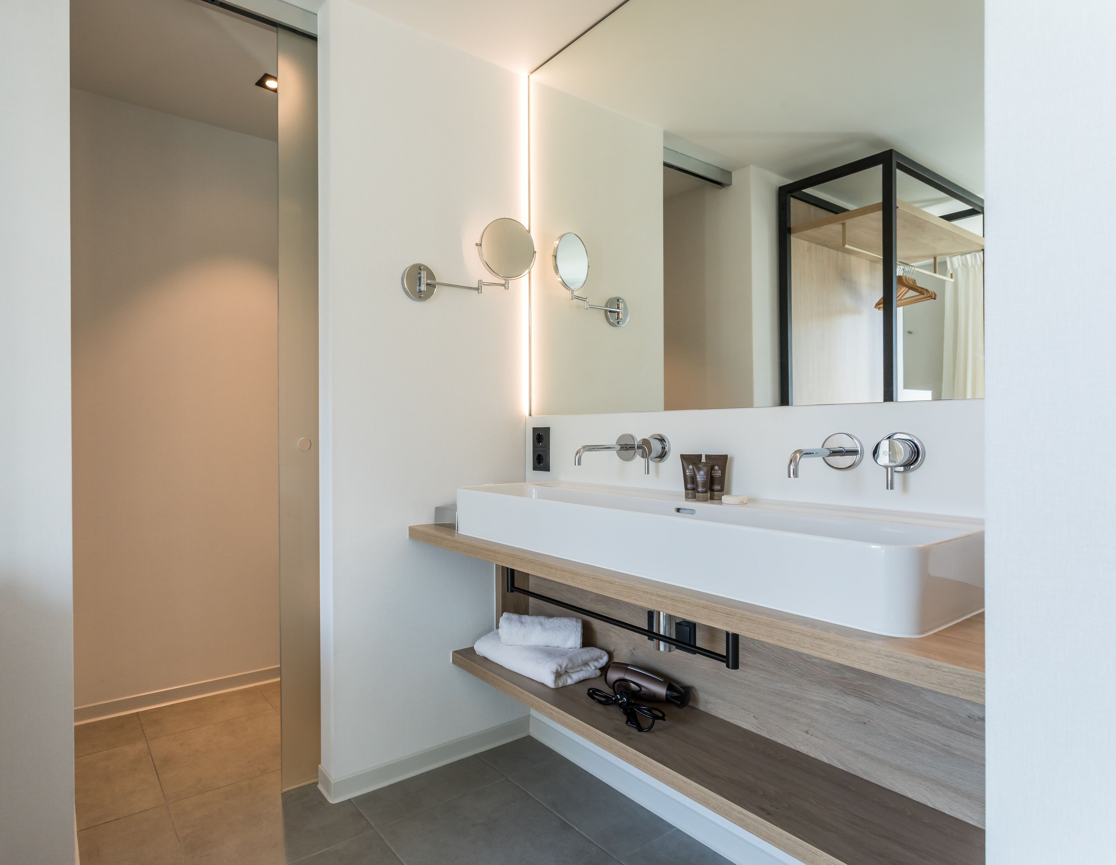 A modern bathroom with a large mirror, two sinks, and a towel rack.