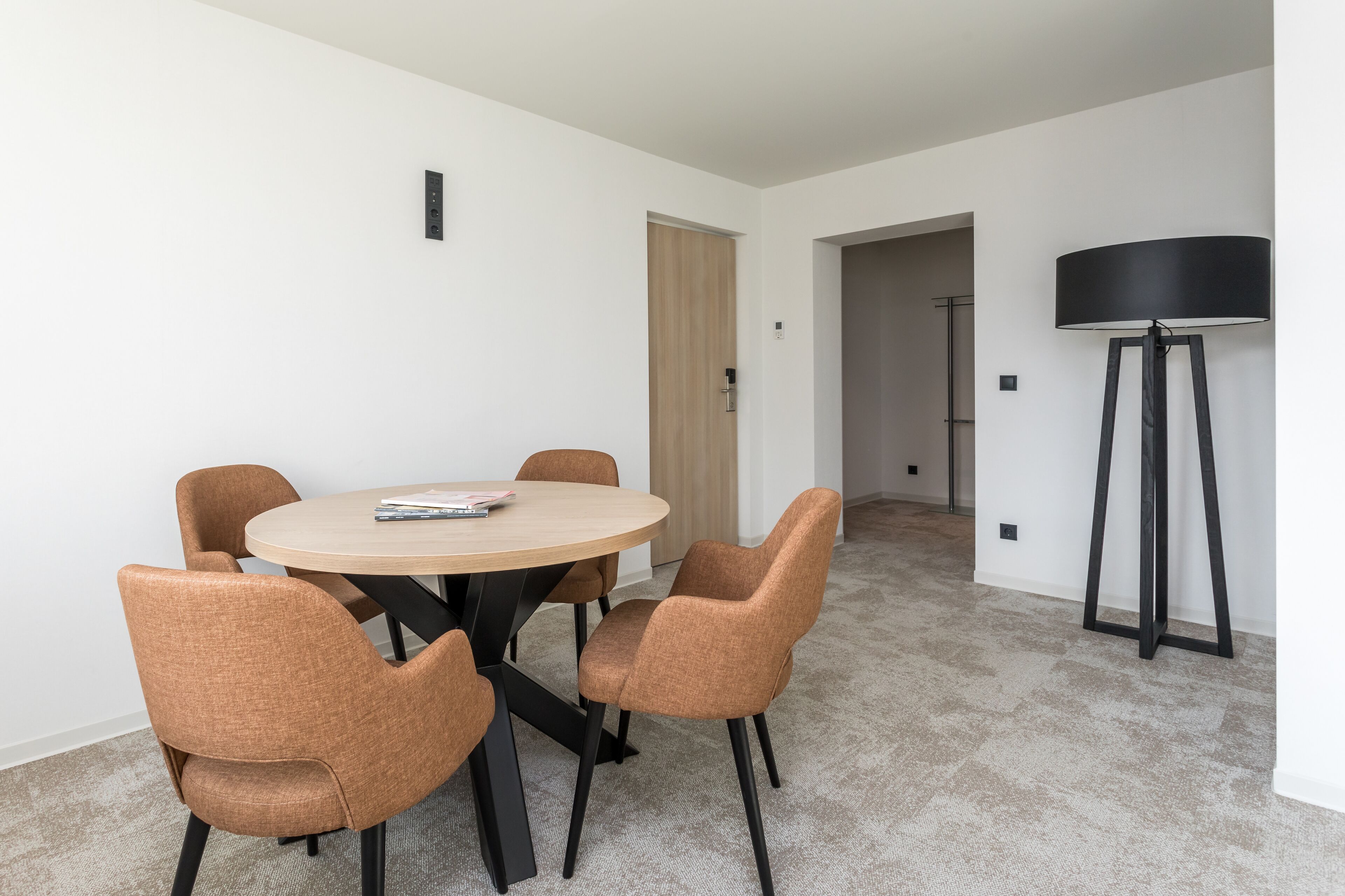 A modern dining area with a round table and four chairs, a standing lamp, and a door leading to another room.