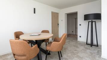 A modern dining area with a round table and four chairs, a standing lamp, and a door leading to another room.