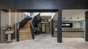 Un moderno vestíbulo de hotel con una escalera, una recepción y un televisor.