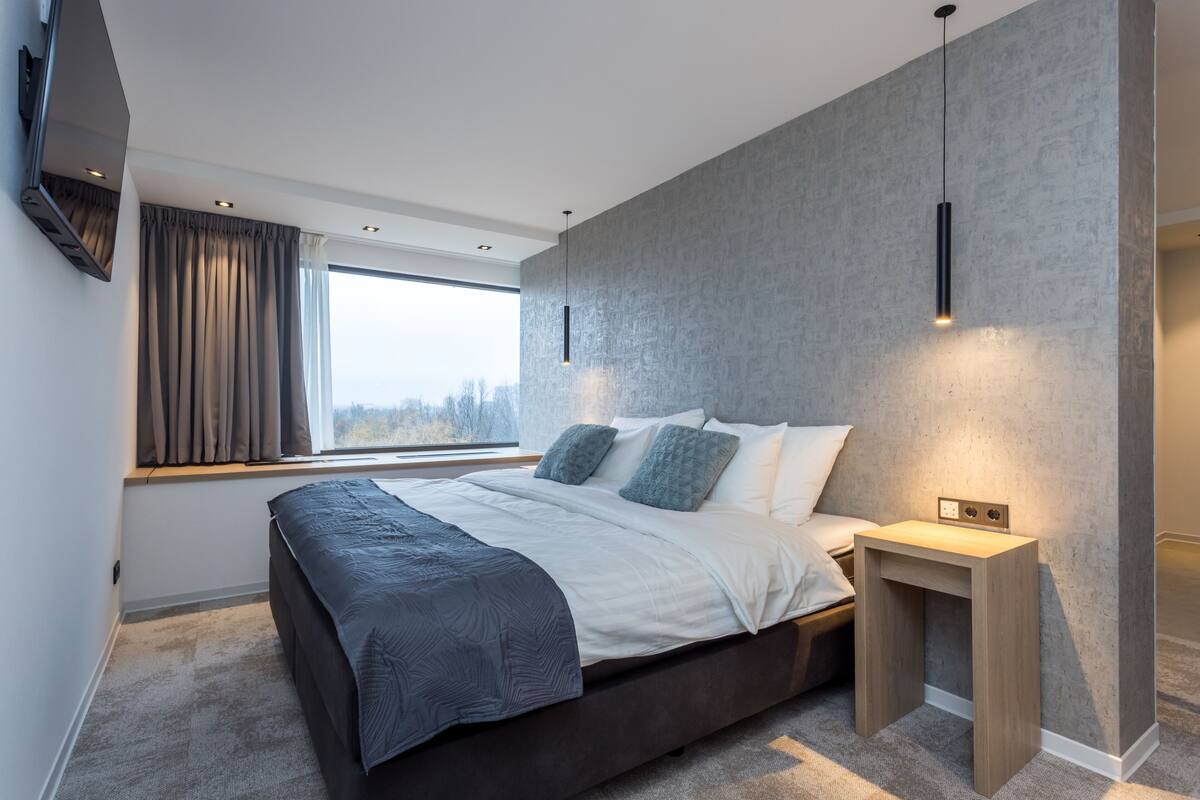 Un dormitorio moderno con una cama grande, una mesita de noche, una ventana con cortinas y un aplique de pared.
