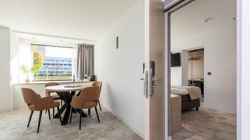 A modern hotel room with a dining area, a bed, and a view of the city.